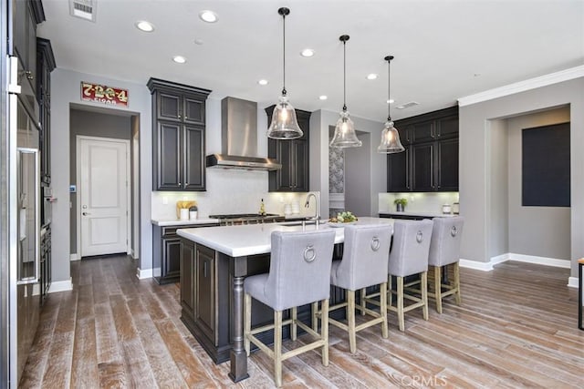 kitchen featuring a kitchen island with sink, light wood-style flooring, visible vents, light countertops, and wall chimney exhaust hood