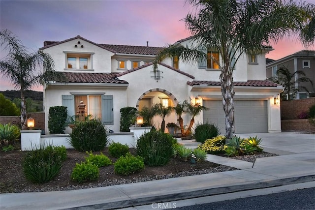 mediterranean / spanish-style home with a garage, a tile roof, driveway, and stucco siding