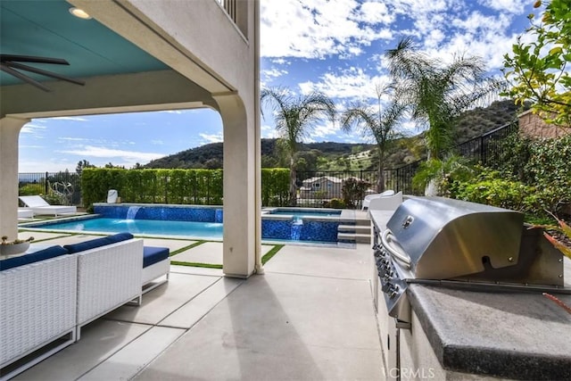 view of swimming pool featuring ceiling fan, a fenced backyard, an outdoor kitchen, and a patio