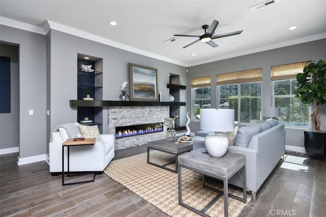 living area with built in features, visible vents, a stone fireplace, wood finished floors, and baseboards