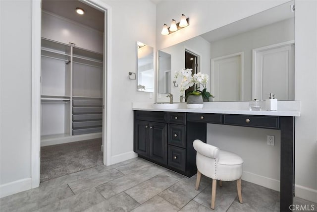 full bath with double vanity, a spacious closet, a sink, and baseboards