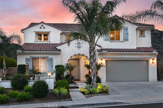 mediterranean / spanish home with a garage, concrete driveway, a tile roof, and stucco siding