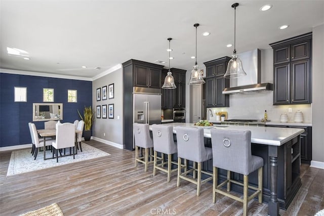 kitchen with a large island, wall chimney exhaust hood, light countertops, light wood-style flooring, and a kitchen breakfast bar