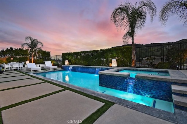 pool at dusk with a pool with connected hot tub, fence, and a patio