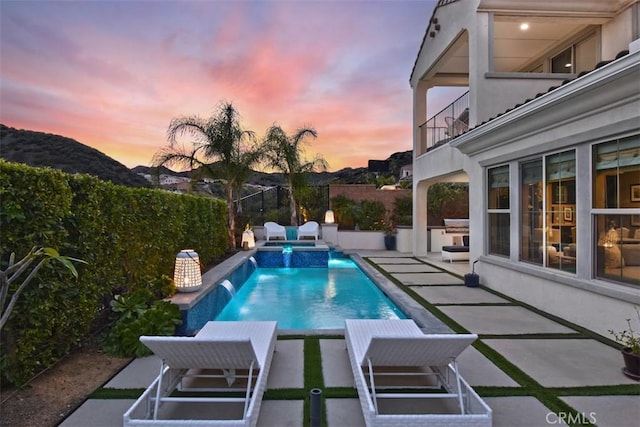 view of swimming pool with a pool with connected hot tub, a fenced backyard, a mountain view, and a patio