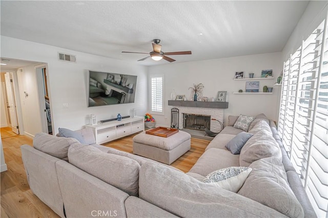 living area with a textured ceiling, light wood-style flooring, a fireplace, visible vents, and a ceiling fan