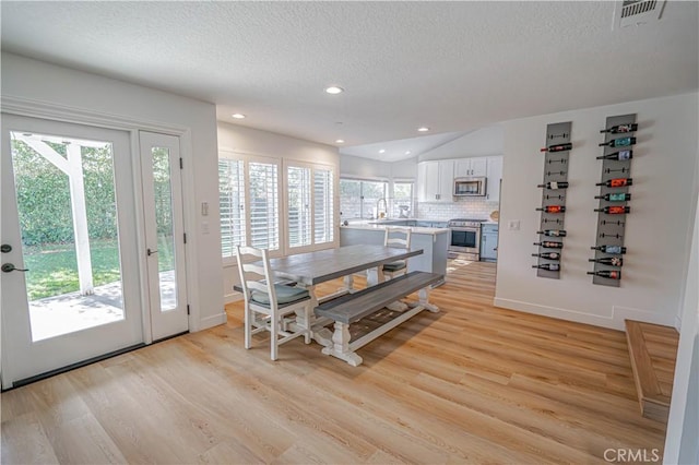 dining space featuring light wood-type flooring, a healthy amount of sunlight, visible vents, and lofted ceiling