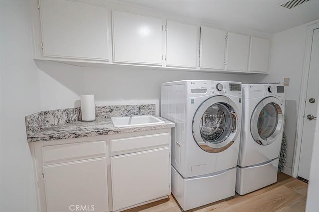 laundry room with light wood-style floors, independent washer and dryer, cabinet space, and a sink