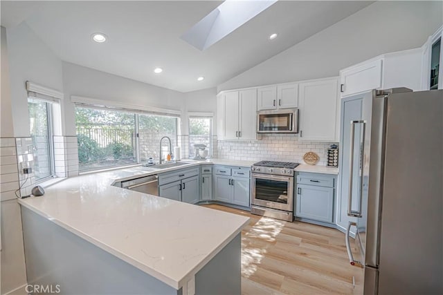 kitchen with a peninsula, a sink, light wood-style floors, appliances with stainless steel finishes, and lofted ceiling with skylight