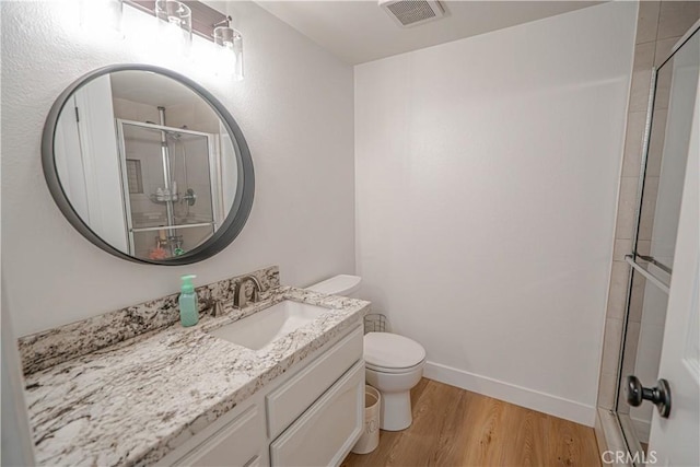 bathroom featuring toilet, wood finished floors, vanity, visible vents, and a stall shower