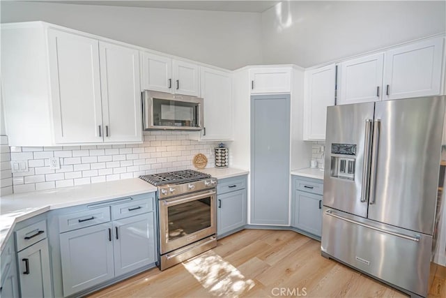 kitchen with stainless steel appliances, tasteful backsplash, light countertops, light wood-style floors, and white cabinets