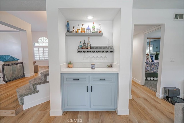 bar with baseboards, visible vents, light wood-style flooring, and a dry bar