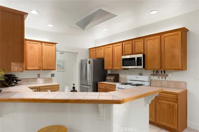 kitchen featuring tile counters, a kitchen breakfast bar, a peninsula, and appliances with stainless steel finishes