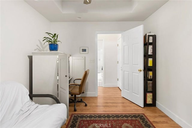 office area featuring a raised ceiling, baseboards, and wood finished floors