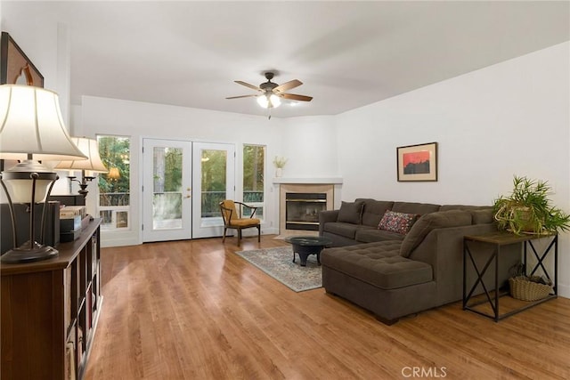 living room featuring ceiling fan, light wood-type flooring, a glass covered fireplace, and french doors