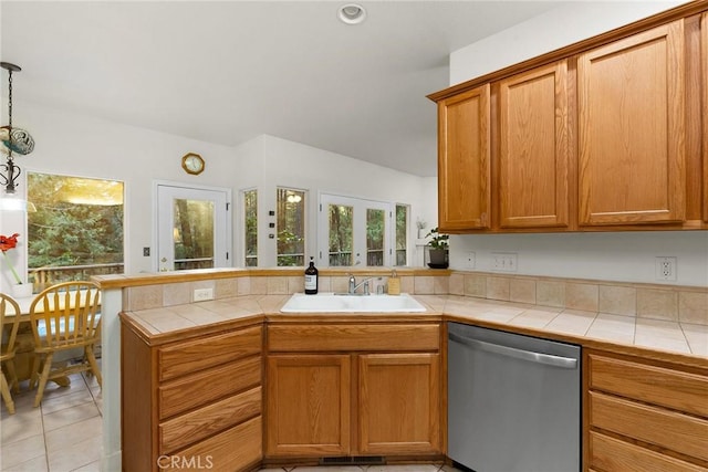 kitchen featuring tile countertops, dishwasher, a peninsula, brown cabinetry, and a sink