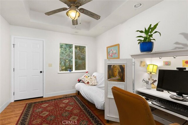 office with ceiling fan, baseboards, a tray ceiling, and wood finished floors