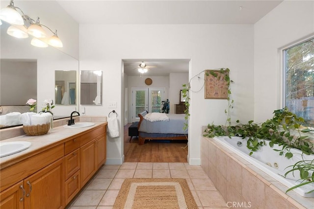 ensuite bathroom featuring tile patterned flooring, connected bathroom, a relaxing tiled tub, double vanity, and a sink