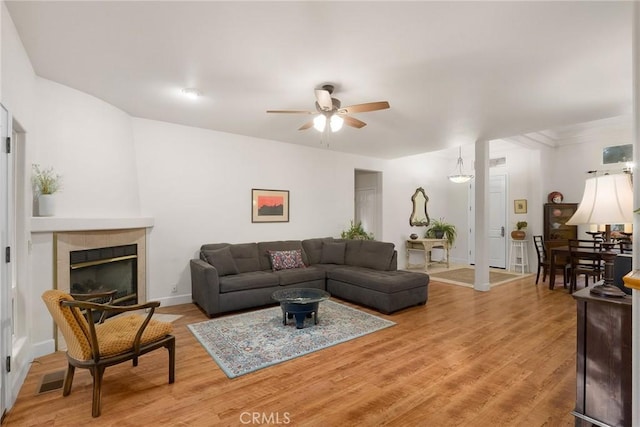 living room featuring a fireplace, light wood-style floors, baseboards, and a ceiling fan