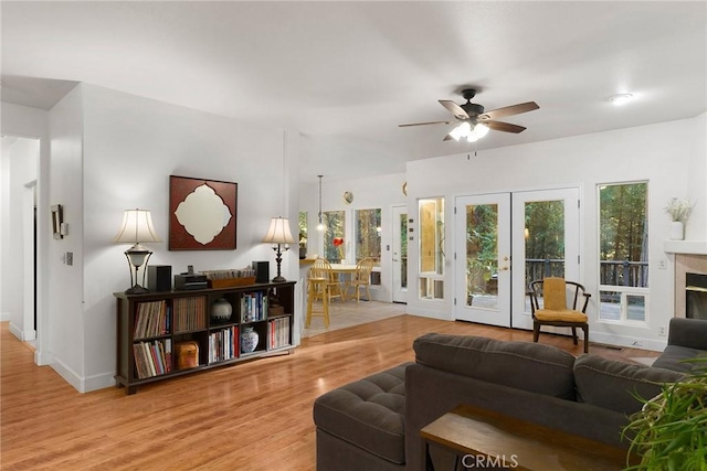 living area with baseboards, ceiling fan, a tiled fireplace, french doors, and wood finished floors