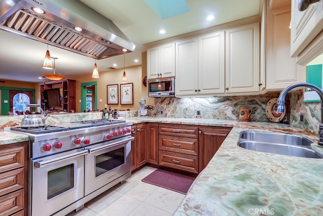 kitchen featuring stainless steel appliances, brown cabinetry, a sink, wall chimney range hood, and light stone countertops