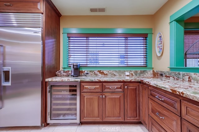 kitchen with light stone counters, beverage cooler, visible vents, brown cabinetry, and stainless steel built in refrigerator