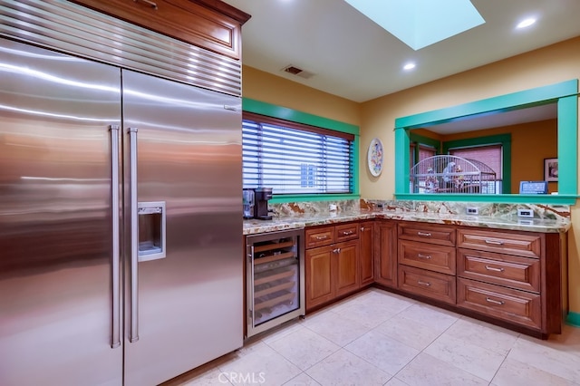 kitchen with a skylight, beverage cooler, visible vents, brown cabinets, and built in fridge