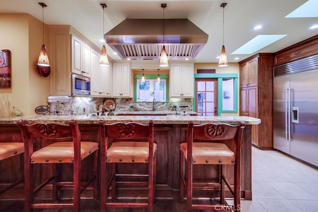 kitchen with light stone counters, decorative light fixtures, backsplash, appliances with stainless steel finishes, and exhaust hood