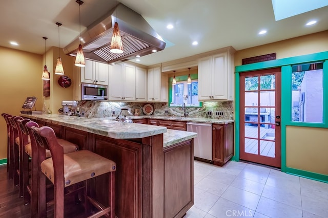 kitchen with stainless steel appliances, decorative backsplash, a peninsula, and island range hood