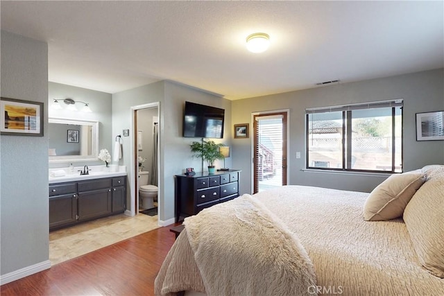 bedroom with visible vents, light wood-style floors, a sink, ensuite bath, and baseboards