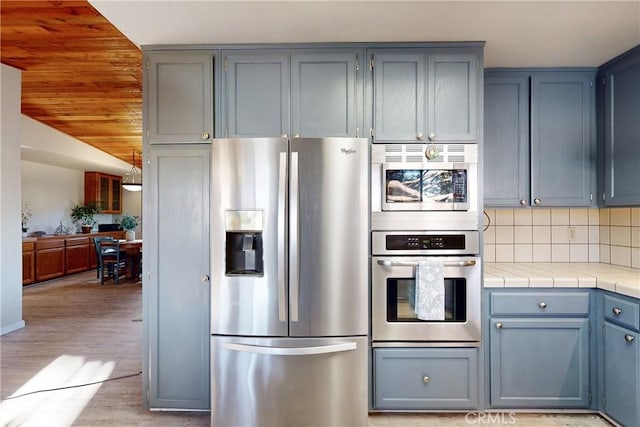 kitchen featuring tile countertops, light wood-style flooring, gray cabinetry, appliances with stainless steel finishes, and backsplash