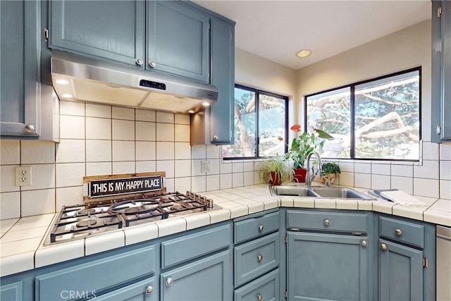 kitchen featuring gas cooktop, under cabinet range hood, a sink, blue cabinetry, and backsplash