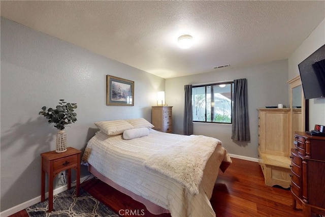 bedroom with dark wood-style floors, baseboards, visible vents, and a textured ceiling