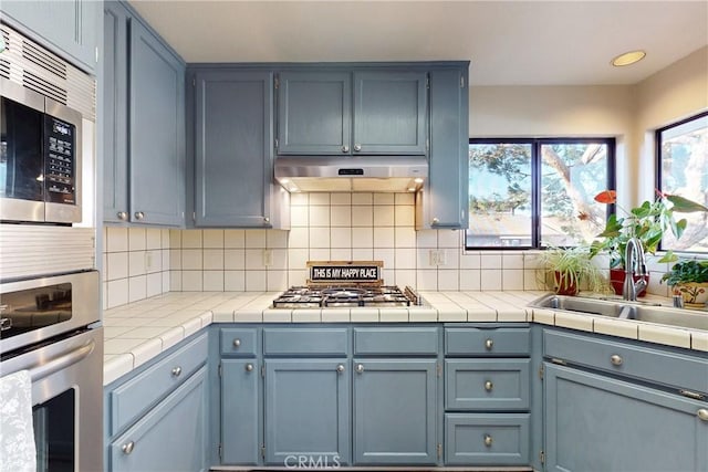 kitchen with appliances with stainless steel finishes, a sink, under cabinet range hood, and decorative backsplash