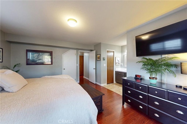 bedroom with ensuite bathroom, baseboards, and wood finished floors