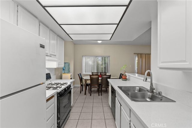 kitchen featuring range with gas stovetop, freestanding refrigerator, under cabinet range hood, white cabinetry, and a sink