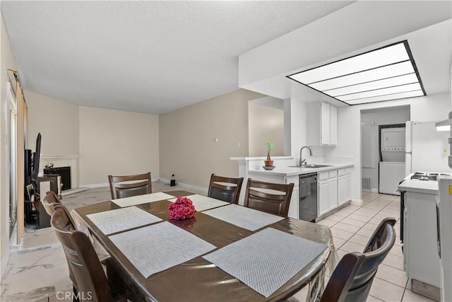 dining room featuring stacked washer / dryer, a fireplace with raised hearth, a textured ceiling, and baseboards