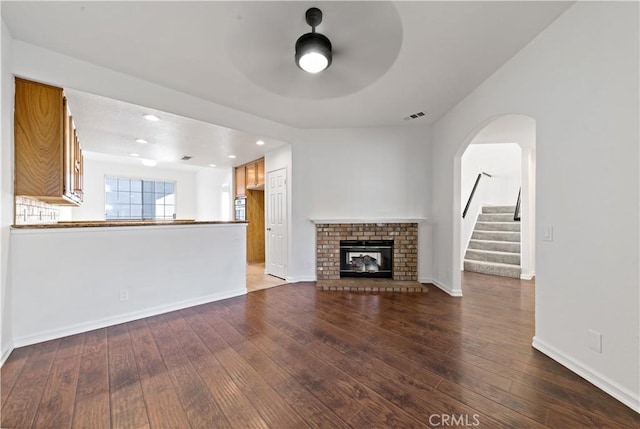 unfurnished living room featuring baseboards, visible vents, a ceiling fan, hardwood / wood-style flooring, and a fireplace