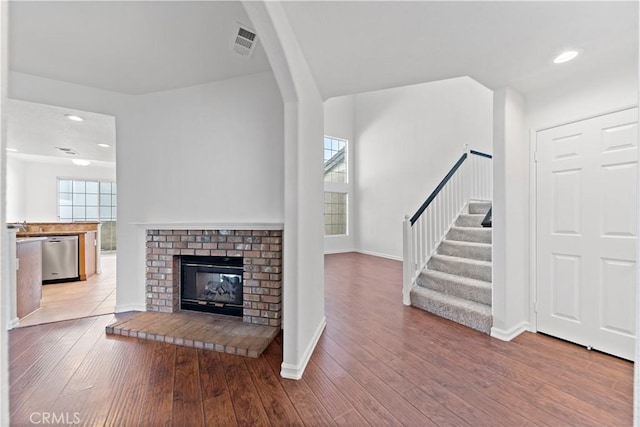 unfurnished living room with visible vents, baseboards, wood-type flooring, stairs, and a brick fireplace