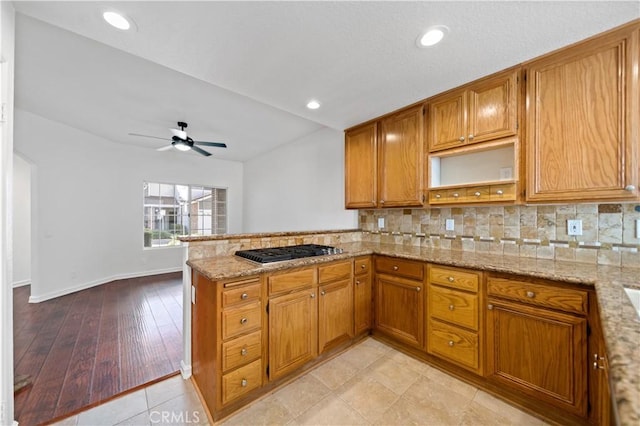 kitchen featuring light stone counters, brown cabinets, stainless steel gas stovetop, backsplash, and a peninsula