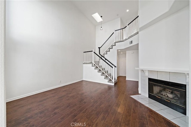 unfurnished living room with a skylight, baseboards, hardwood / wood-style flooring, stairs, and a fireplace