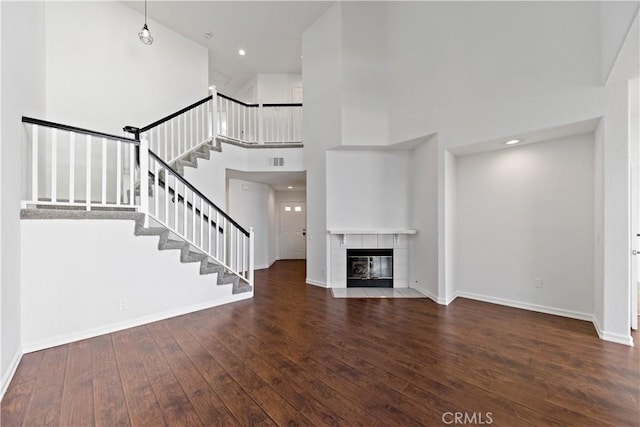 unfurnished living room with wood-type flooring, visible vents, a tile fireplace, baseboards, and stairs