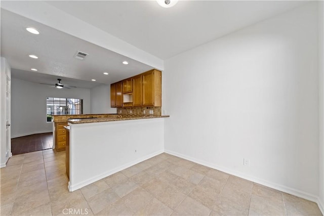 kitchen featuring tasteful backsplash, visible vents, baseboards, brown cabinets, and a peninsula