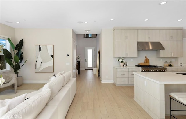 kitchen with recessed lighting, light countertops, light wood-style floors, under cabinet range hood, and open floor plan