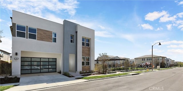 contemporary house with stucco siding, a residential view, a garage, and concrete driveway