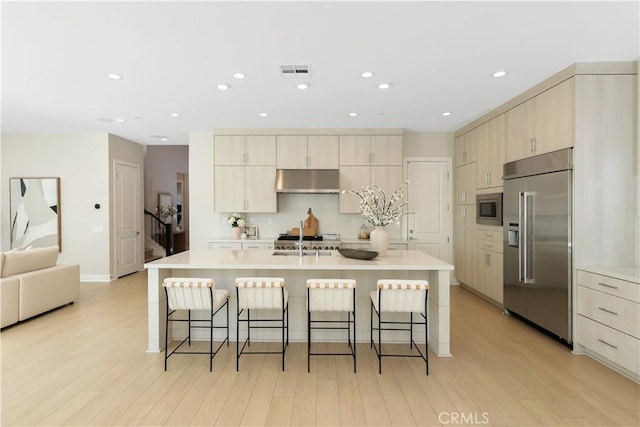 kitchen with visible vents, under cabinet range hood, a kitchen breakfast bar, light countertops, and built in appliances