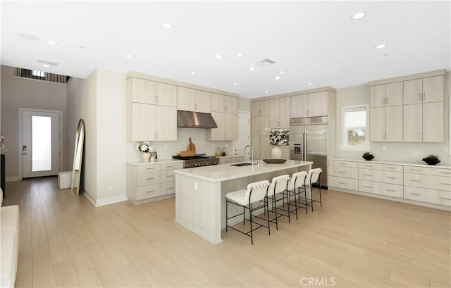 kitchen featuring stainless steel built in fridge, a kitchen bar, under cabinet range hood, a sink, and range