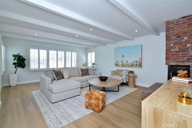 living room featuring a fireplace, beamed ceiling, baseboards, and wood finished floors