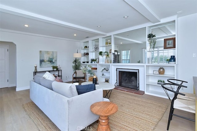 living area featuring arched walkways, a fireplace with raised hearth, beamed ceiling, and wood finished floors