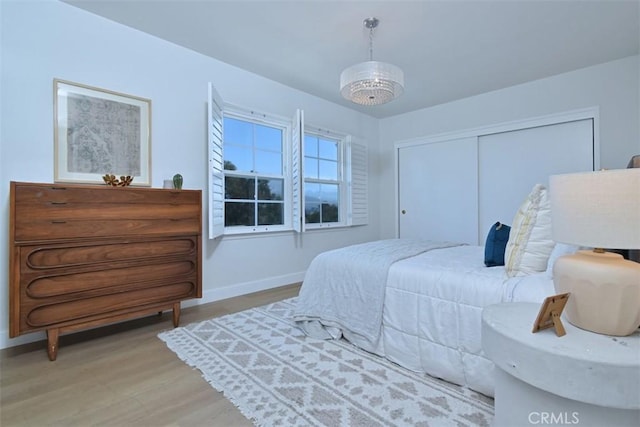 bedroom featuring a chandelier, a closet, baseboards, and light wood finished floors